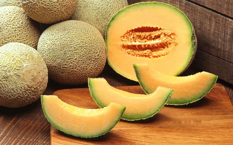 Whole and sliced cantaloupes on a wooden board